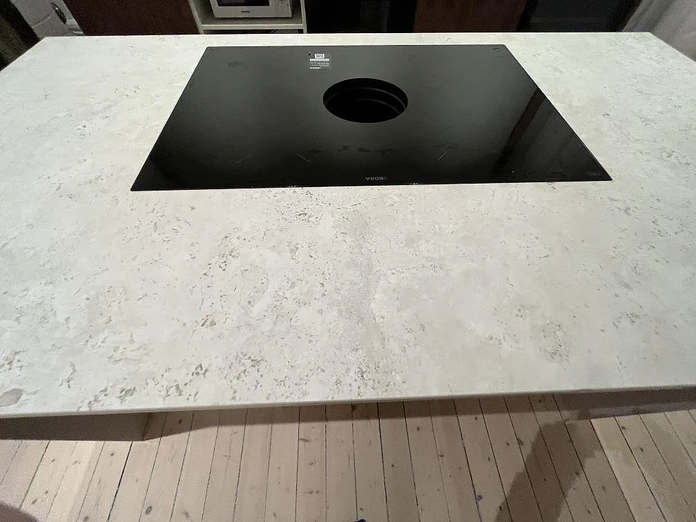 Närbild på matt Dekton TK05 Sabbia som köksbänkskiva runt induktionshäll på köksö i Stockholm.