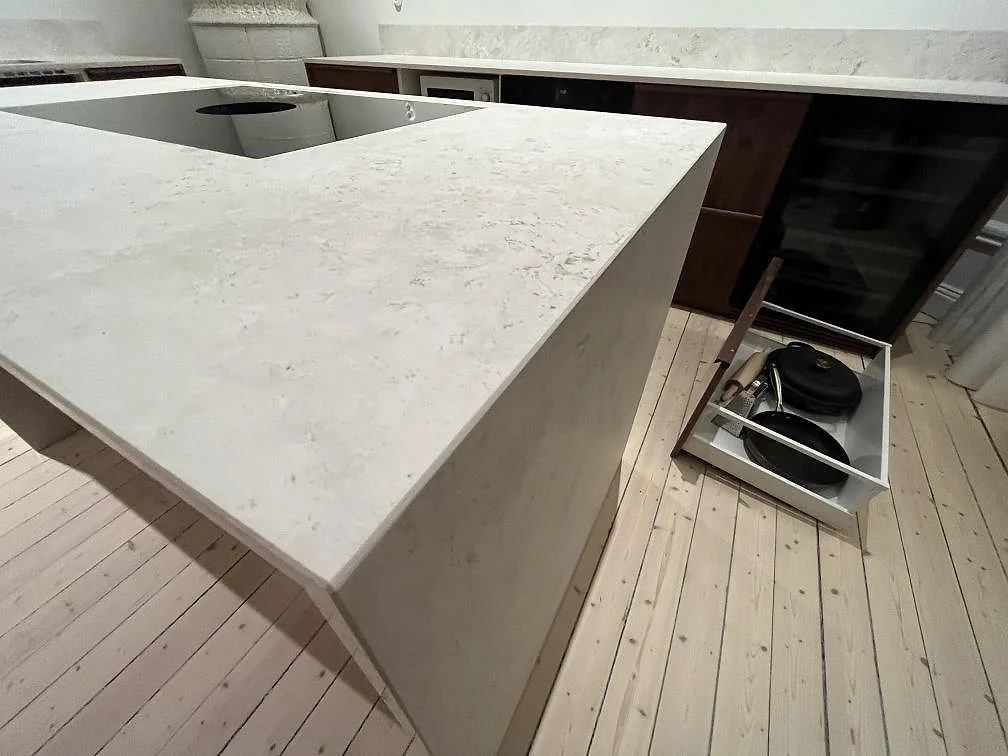 Detalj av köksö i matt Dekton TK05 Sabbia med tjock kant, mörk träinredning och väggbänk i Stockholm.