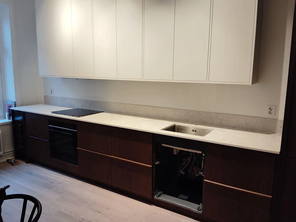 Köksbänkskiva i matt Dekton Tk05 Sabbia med häll, diskho och låg stänkkant i ett kök i Stockholm.