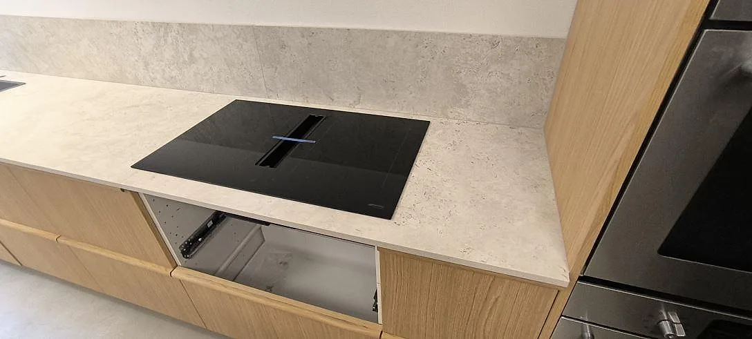Närbild på matt Dekton Tk05 Sabbia köksbänkskiva med svart häll och ljus stenstruktur i Stockholm.