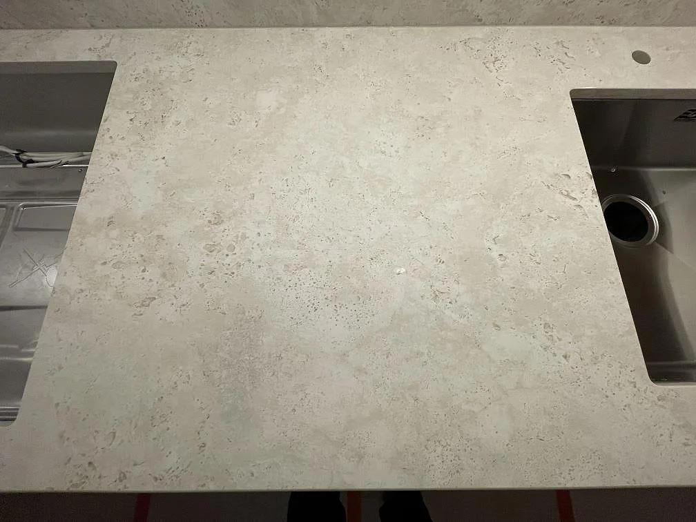 Närbild uppifrån på matt Dekton TK05 Sabbia köksbänk i sandbeige keramik med synlig kornig yta, rostfri underlimmad diskho och blandarhål i ett kök i Stockholm.
