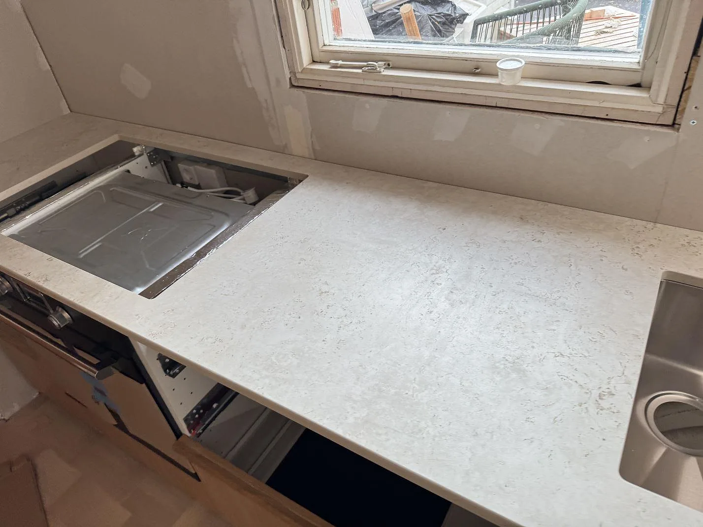Närbild av matt keramisk Dekton Tk05 Sabbia med hällöppning, diskho och ljus stenstruktur i köket i Tollered.