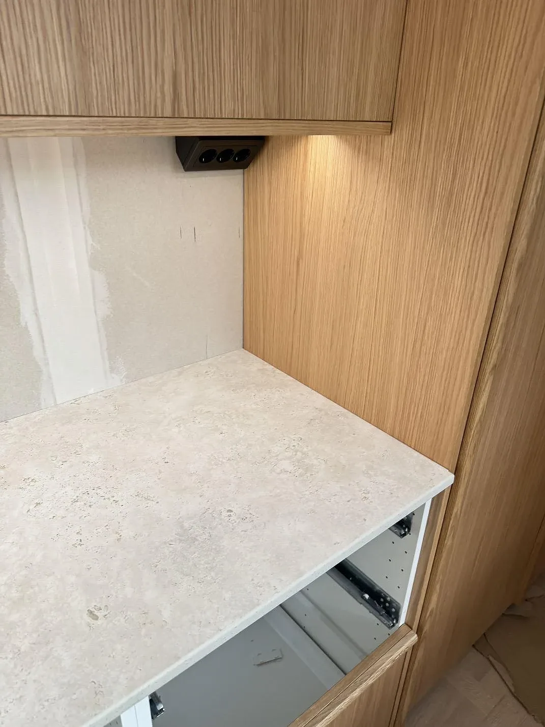 Sidodetalj av den ljusa köksbänkskivan i matt keramisk Dekton Tk05 Sabbia mot träinredning i Tollered.