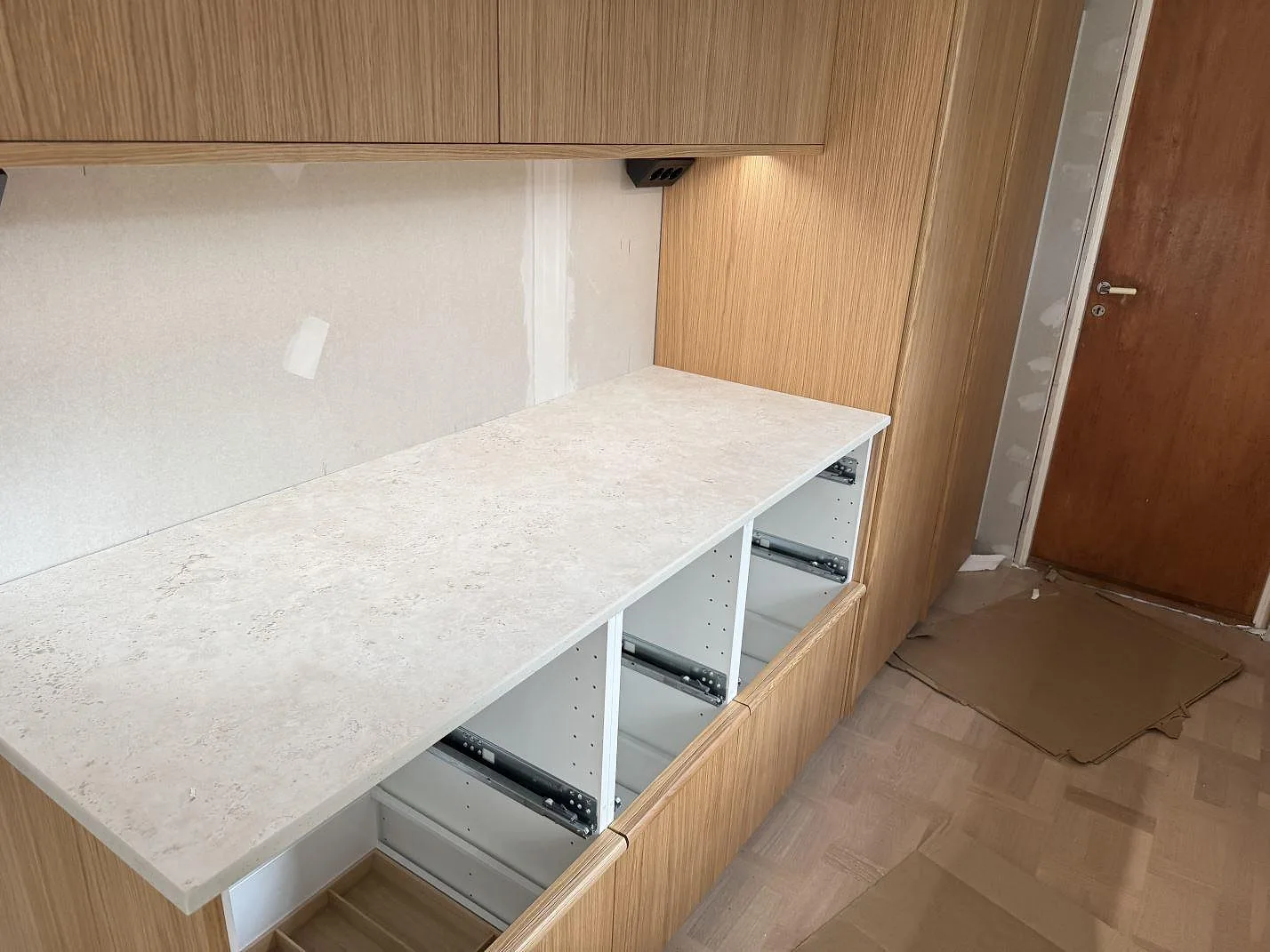 Rak arbetsyta i matt keramik, Dekton Tk05 Sabbia, mot träinredning och öppna köksstommar i Tollered.