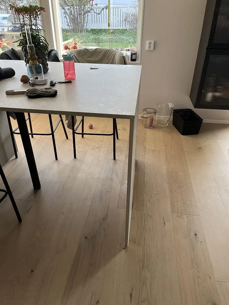 Sidovy av lång köksö i matt Dekton Tk05 Sabbia med barstolar, fönsterljus och ljust trägolv i Trångsund.