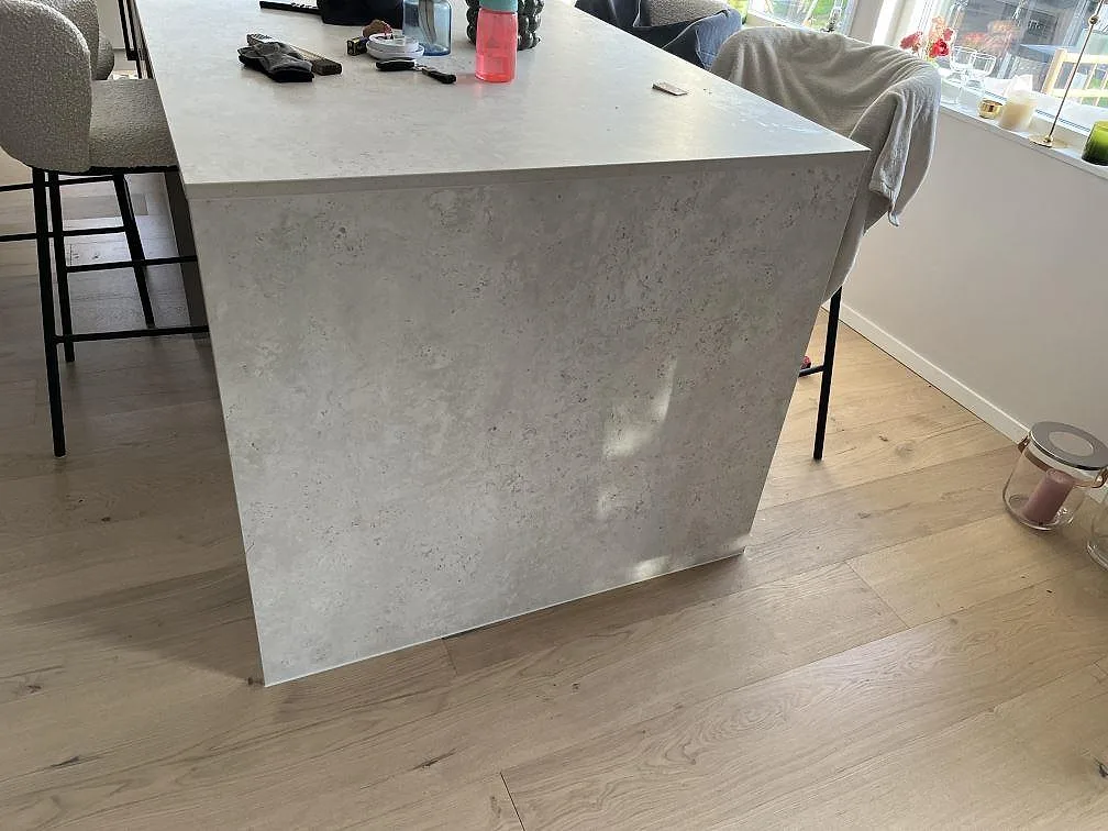 Närbild på köksö med sidostycke i matt Dekton Tk05 Sabbia, ljus keramik och trägolv i ett kök i Trångsund.