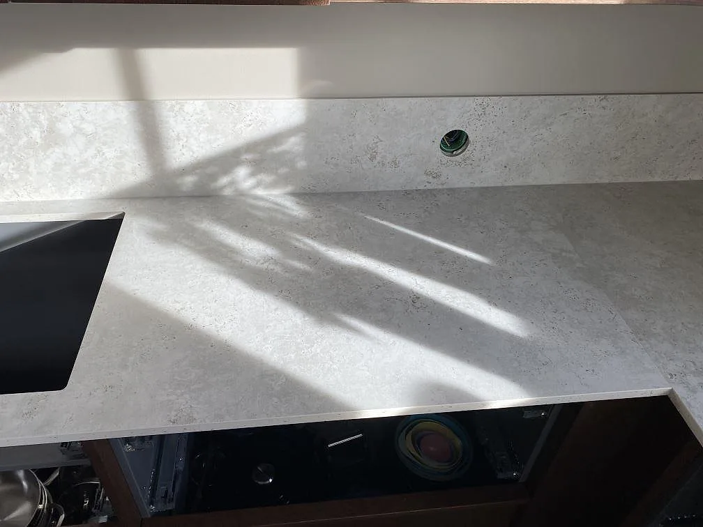 Detalj av matt Dekton Tk05 Sabbia på köksbänk med ljus stenstruktur och stänkskydd i Väjern.