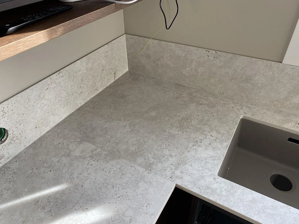 Hörn av köksbänkskiva i matt Dekton Tk05 Sabbia med stänkskydd och synlig diskho i Väjern.
