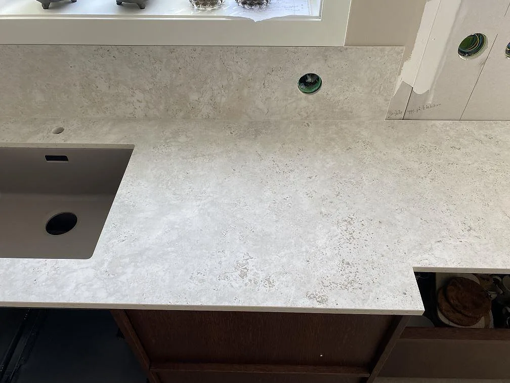 Köksbänkskiva i matt Dekton Tk05 Sabbia med diskho, stänkskydd och eluttag under fönster i Väjern.