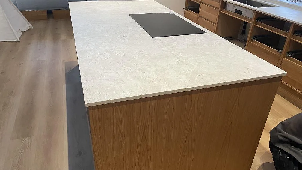 Köksö i matt Dekton Tk05 Sabbia med svart häll och trästommar under montering i Vejle.