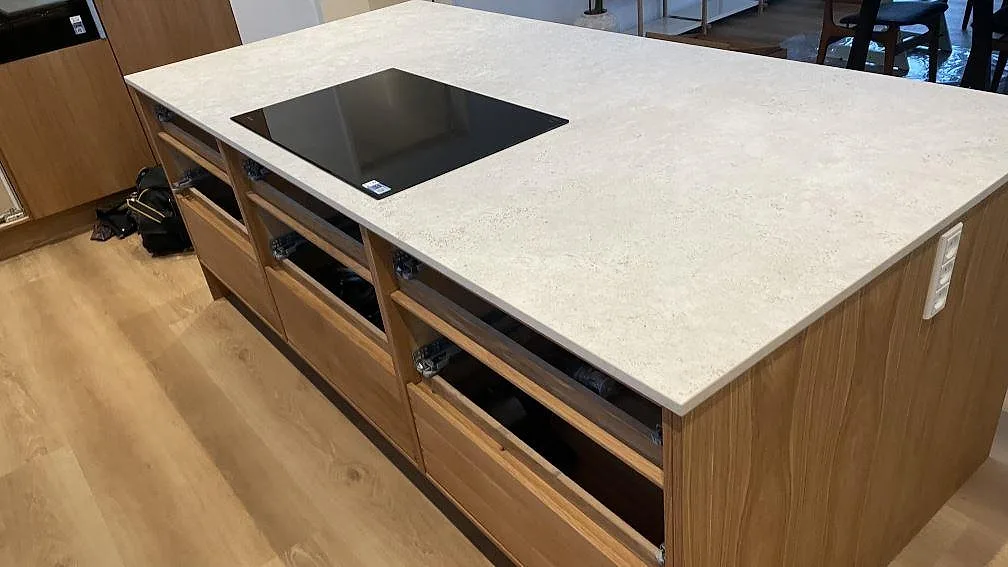 Köksö med ljus keramikskiva i Dekton Tk05 Sabbia och svart häll, fotograferad under montering i Vejle.