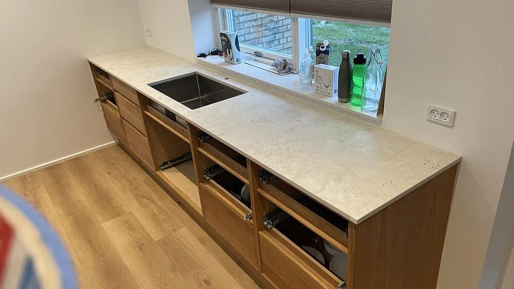 Bänkskiva längs fönster i matt Dekton Tk05 Sabbia med diskho och öppna trästommar i köket i Vejle.