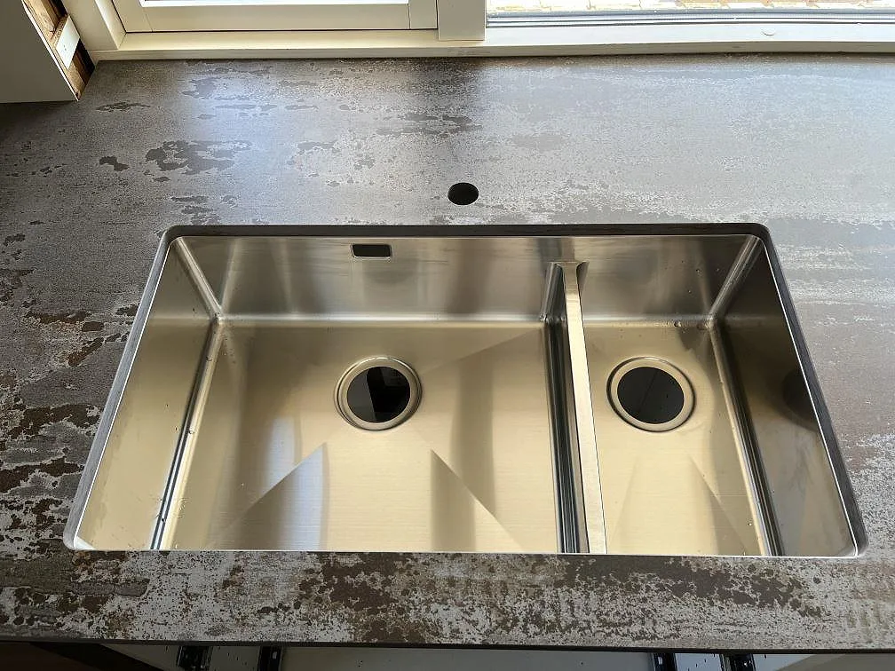 Detalj av underlimmad rostfri dubbeldiskho i en mörk Dekton Trilium bänkskiva i ett kök i Åstorp.