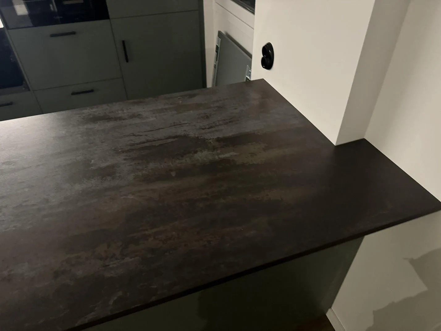 Närbild på köksö i matt Dekton Trilium med mörk stenstruktur och grön köksinredning i Helsingborg.