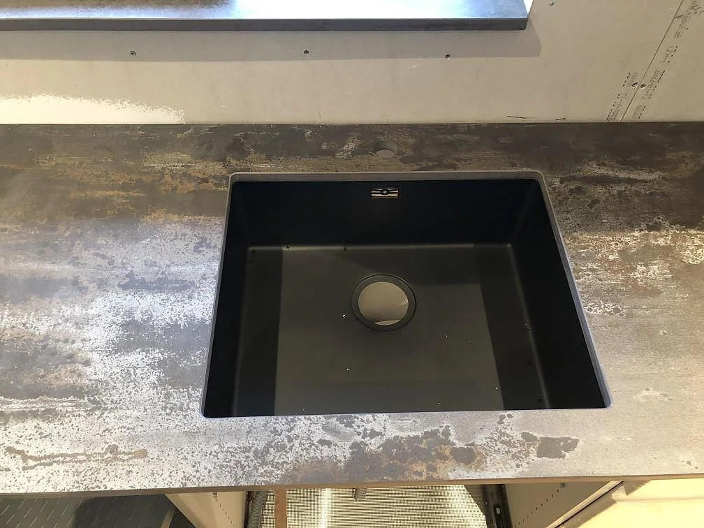 L-formad köksbänk i Dekton Trilium som viker runt hörnet med urtag för häll och en fönsterbänk i samma sten, kök i Jonstorp.