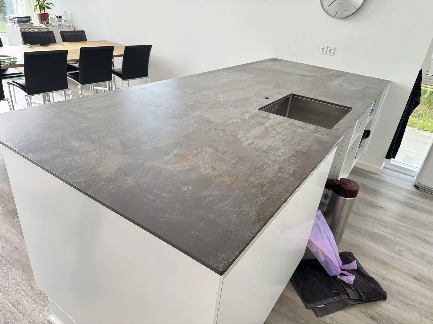 Bred vy över köksö med matt Dekton Trilium som bänkskiva, rostfri diskho och vita stommar i Snekkersten.