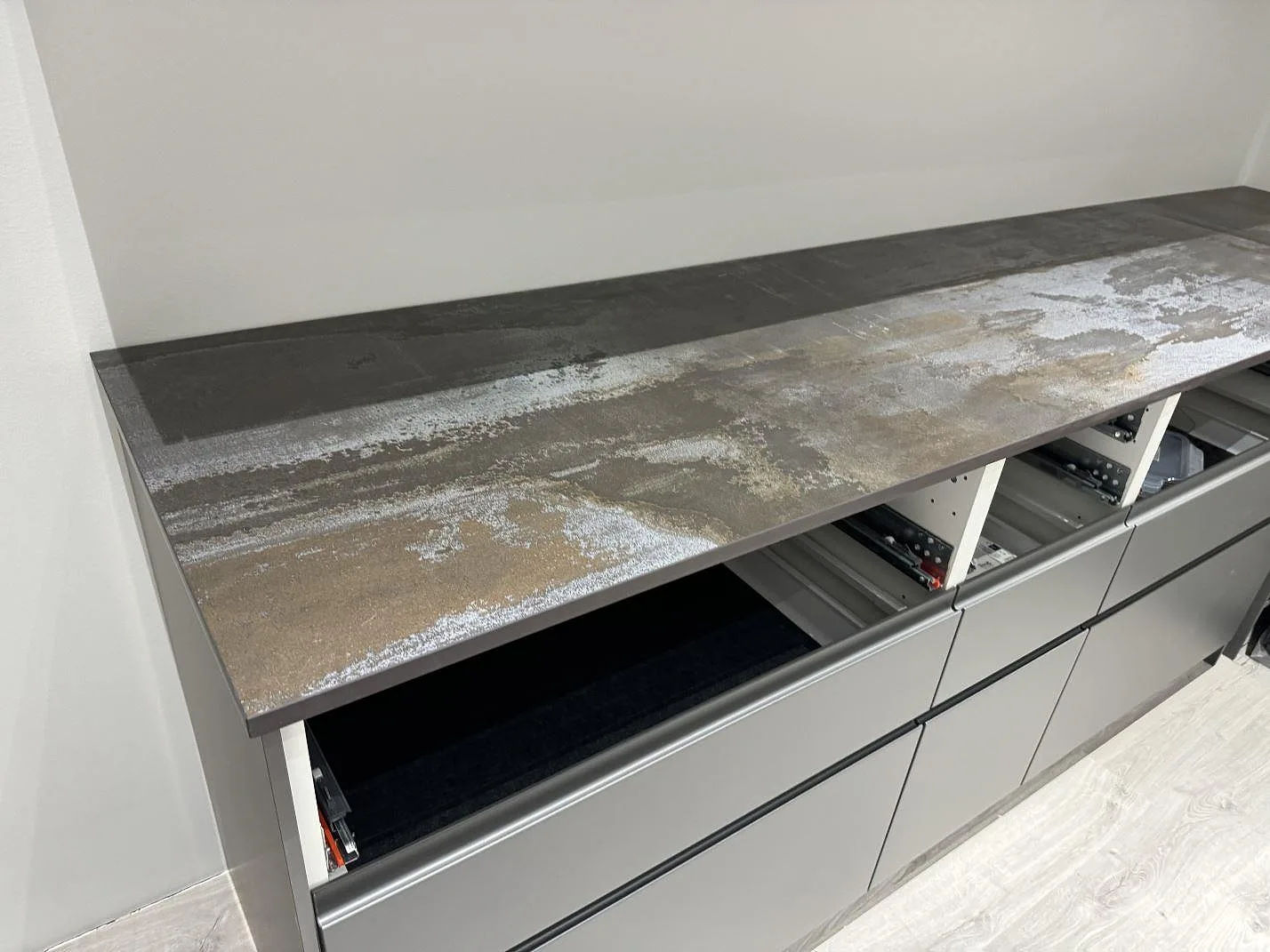 Lång köksbänkskiva i matt Dekton Trilium ovanpå grå köksstommar i Torslanda.
