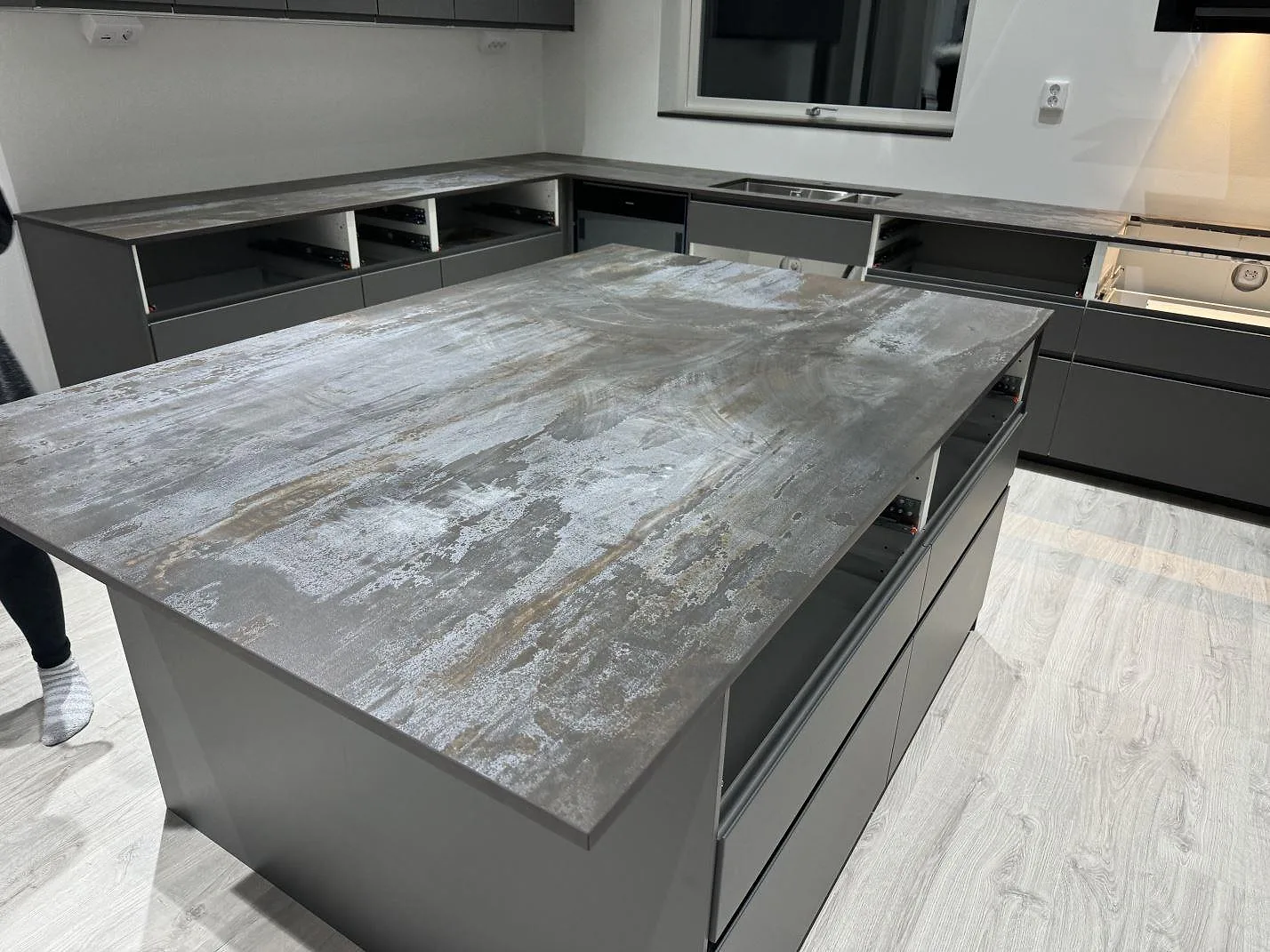 Köksö och väggbänkar i matt Dekton Trilium keramik, med synlig diskho och hällzon i köket i Torslanda.