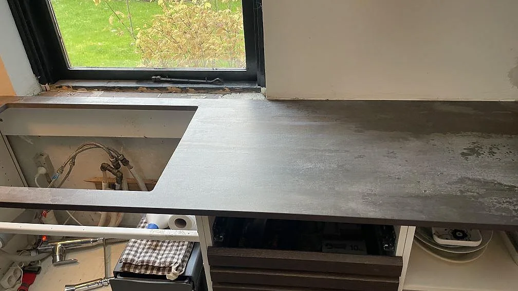 Lång köksbänkskiva i matt Dekton Trilium under fönster med rostbrun keramisk yta i Vedbæk.