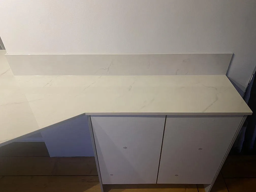 Polerad Dekton Tundra 19 bänkskiva med låg stänkkant, vit stomme och grå ådring i ett kök under montering i Åsa.