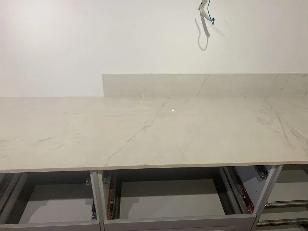 Rak bänkyta i polerad Dekton Tundra 19 med diskret grå ådring, öppna skåpstommar och matchande stänkskydd i Åsa.