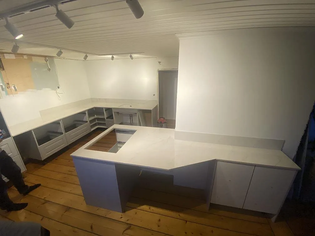 Köksbänkskiva och köksö i polerad Dekton Tundra 19 med grå ådring, lågt stänkskydd och vita stommar under montering i Åsa.