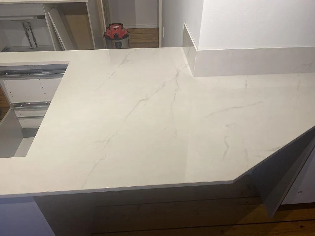 Närbild på polerad Dekton Tundra 19 köksö med mjuk grå ådring och anslutande bänkskiva runt väggparti i Åsa.