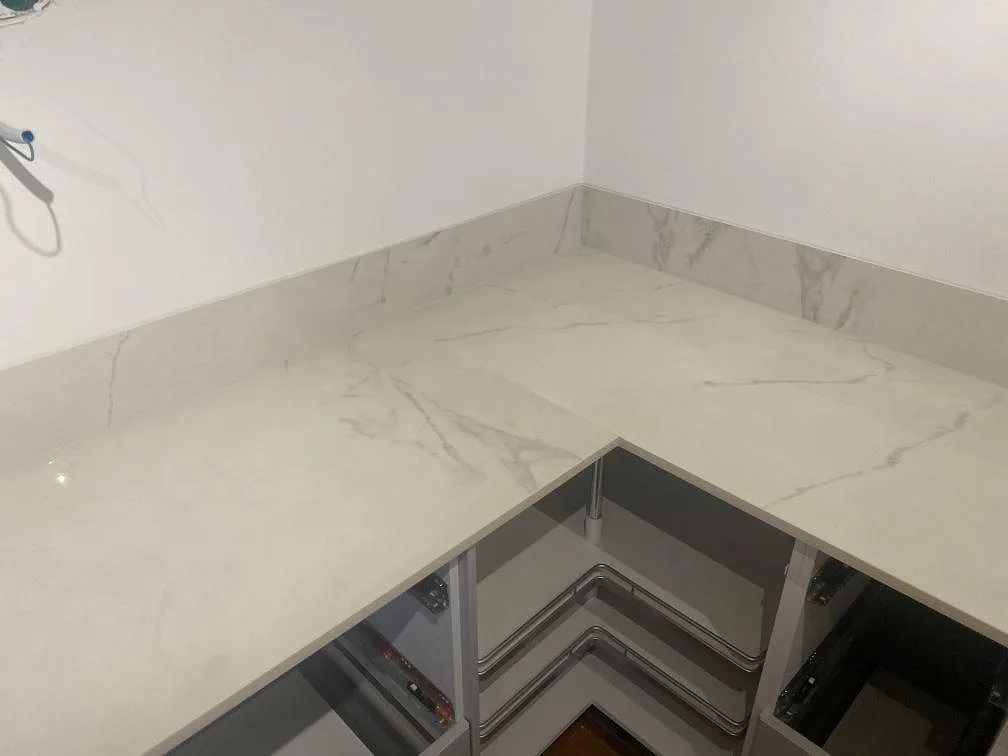 Hörnparti av polerad Dekton Tundra 19 med grå ådring, låg stänkkant och öppna köksstommar under montering i Åsa.