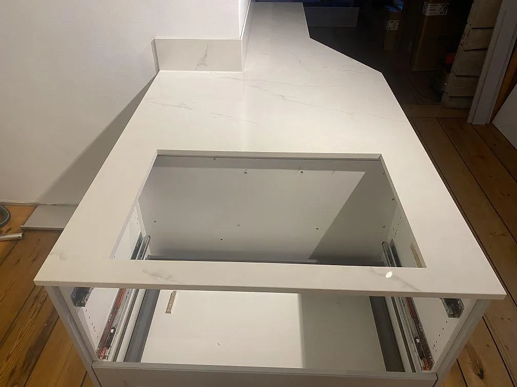 Köksö i polerad Dekton Tundra 19 med urtag för häll och ljus grå ådring i ett kök under montering i Åsa.