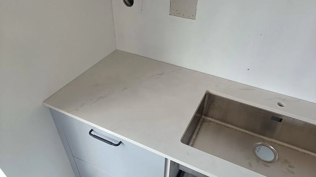 Perimeterbänk i vit Dekton Tundra med underlimmad rostfri diskho och uppvikt stänkkant i ett kök i Asmundtorp.