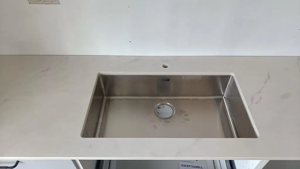 Närbild på underlimmad rostfri diskho i en polerad Dekton Tundra bänkskiva i Asmundtorp.