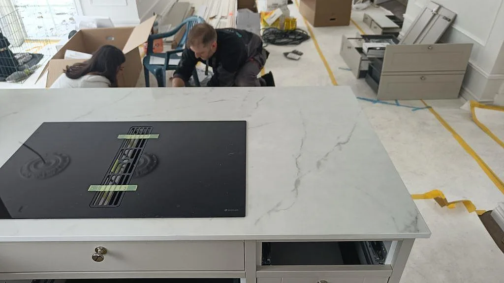 Köksö i polerad vit Dekton Tundra med induktionshäll och diskret grå ådring i ett kök i Borås.