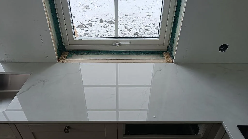 Köksbänkskiva i vit Dekton Tundra vid fönstret med underlimmad rostfri diskho i ett kök i Borås.
