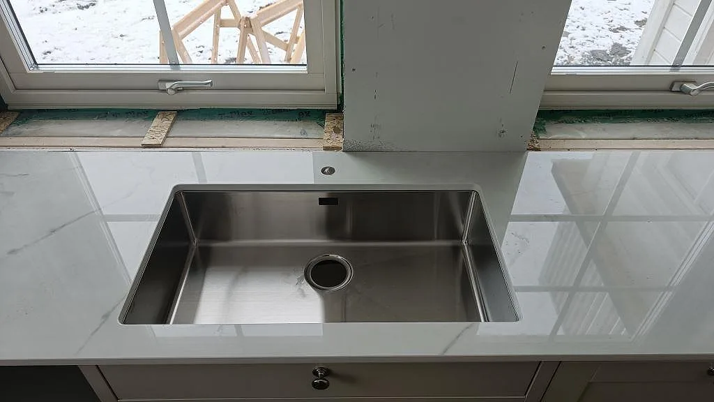 Underlimmad rostfri diskho i en bänkskiva av polerad vit Dekton Tundra i ett kök i Borås.