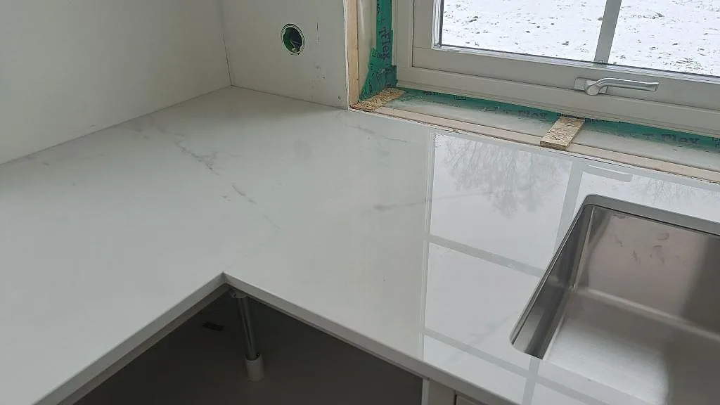Hörnparti av polerad Dekton Tundra bänkskiva med underlimmad rostfri diskho vid fönstret i ett kök i Borås.