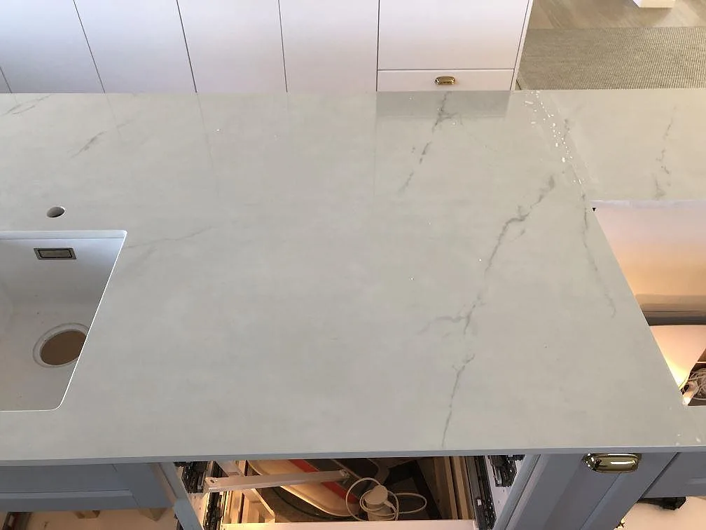 Köksbänkskiva i Dekton Tundra med diskhourtag och blank polerad yta, ljus marmorlik ådring, i ett kök i Halmstad.