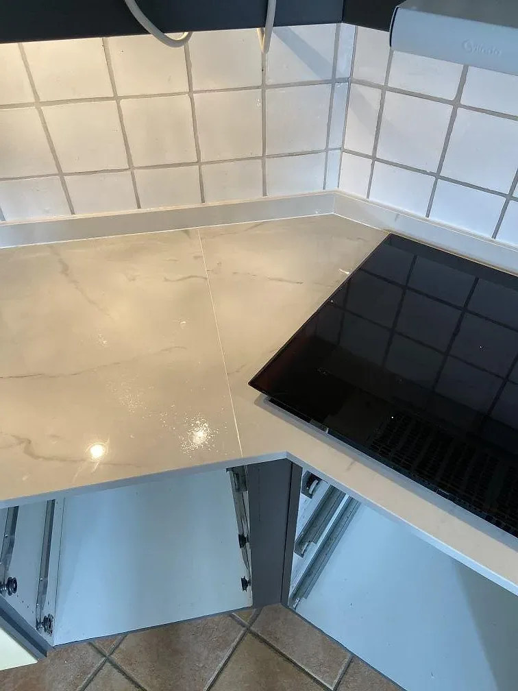 Detalj av svart häll infälld i en polerad köksbänkskiva av Dekton Tundra 19 med marmorerad keramikyta i Löddeköpinge.