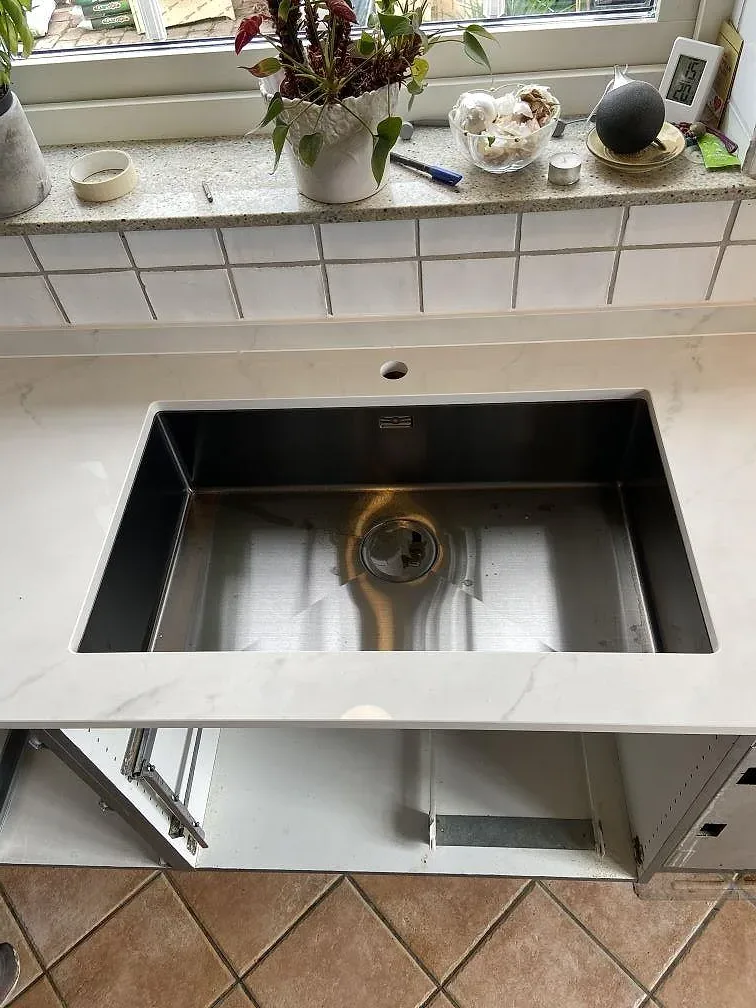 Underlimmad rostfri diskho i en vit marmorerad köksbänkskiva av polerad Dekton Tundra 19 i Löddeköpinge.