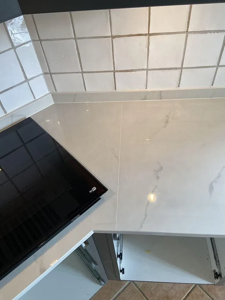 Köksbänkskiva i polerad Dekton Tundra 19 med svart häll, ljus ådring och matchande kant mot kakel i Löddeköpinge.