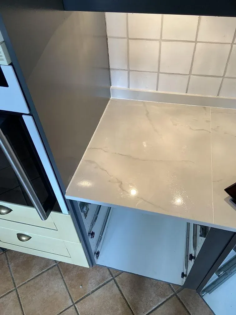 Närbild på köksbänkskiva i polerad Dekton Tundra 19 med vit ådring, svart häll och ljusa köksfronter i Löddeköpinge.