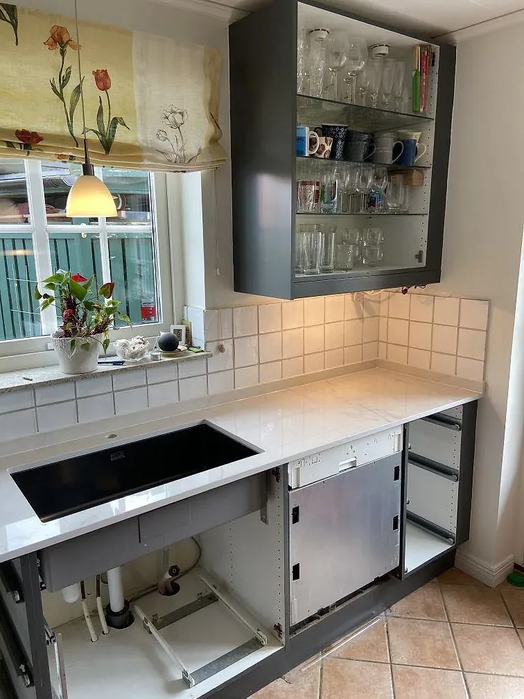 Polerad Dekton Tundra 19 som köksbänkskiva med svart häll, öppna skåpstommar och matchande stänkskydd i Löddeköpinge.
