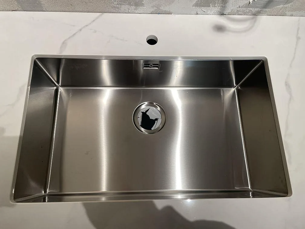 Närbild på underlimmad rostfri diskho monterad under den gräddvita Dekton Tundra-bänkskivan i ett kök i Rydebäck.