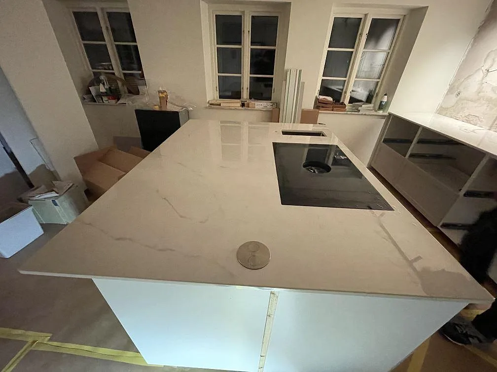 Eye-level vy över köksön i polerad Dekton Tundra med BORA-häll och mjuk grå ådring i ett kök under montering i Rydebäck.