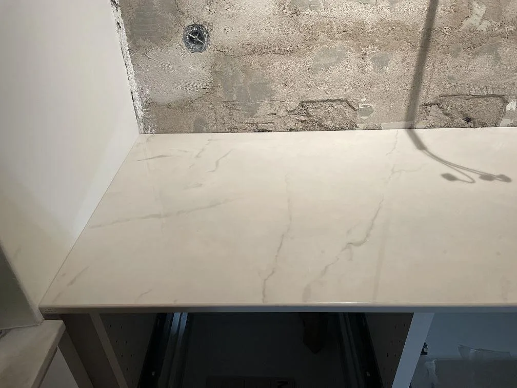 Köksbänkskiva i marmorlik Dekton Tundra mot oputsad betongvägg under montering i ett kök i Rydebäck.