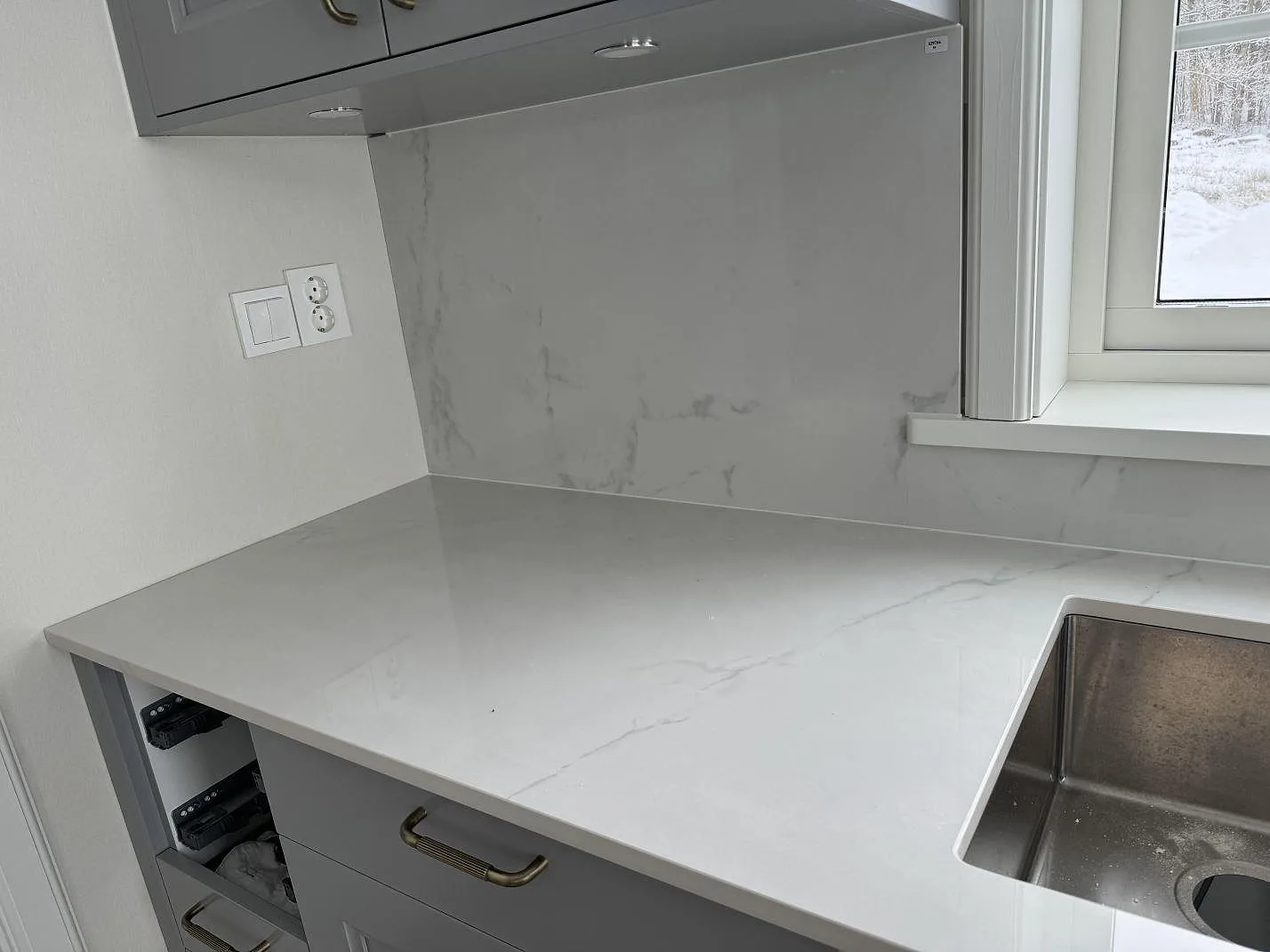 Polerad köksbänkskiva i Dekton Tundra 19 med underlimmad rostfri diskho och stänkskydd vid fönster i Stråvalla.