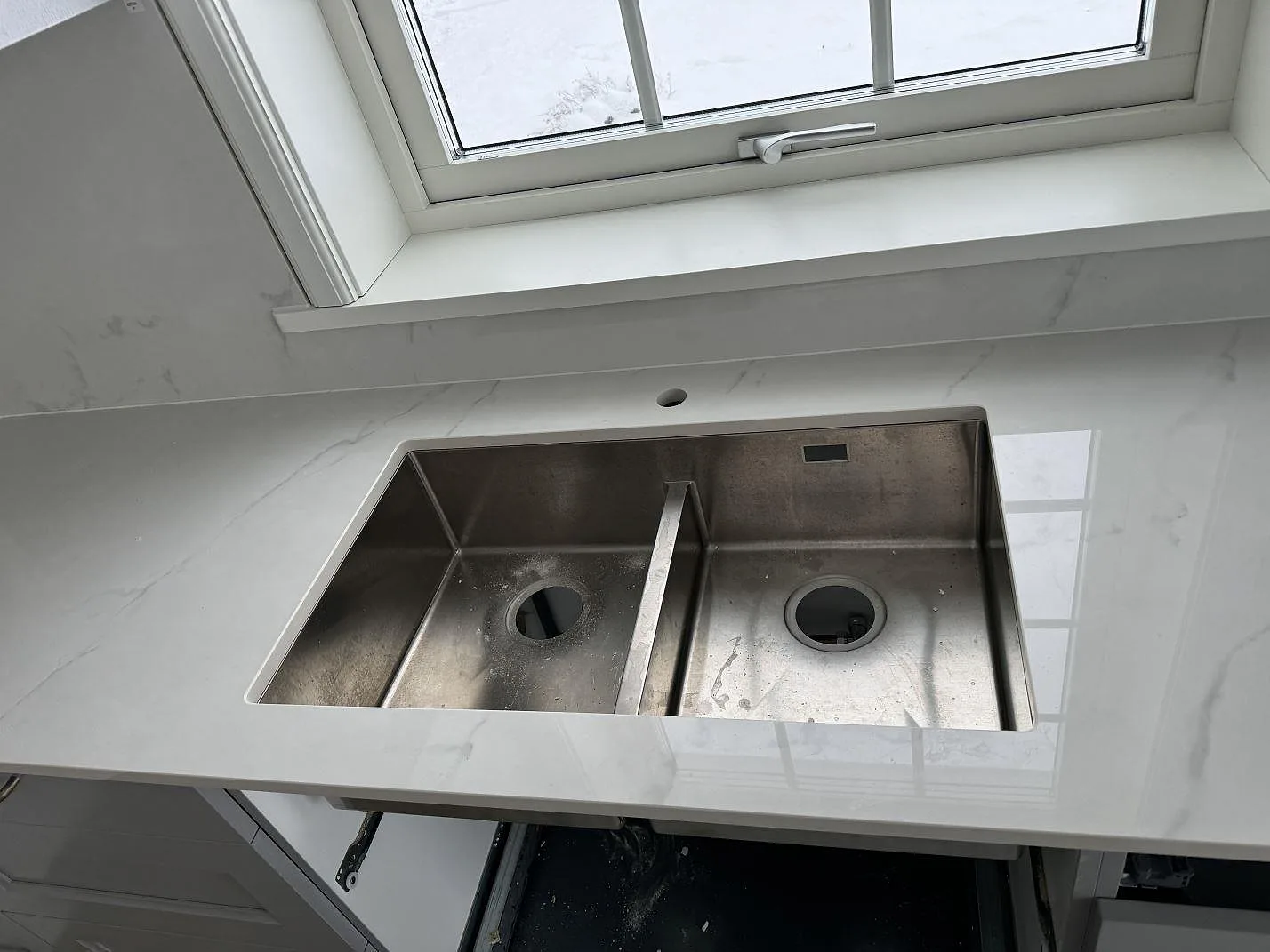 Närbild på underlimmad rostfri diskho i polerad Dekton Tundra 19 med tapphål och stänkskydd i ett kök i Stråvalla.
