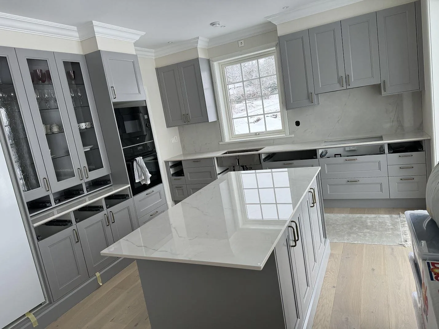 Köksbänkskiva och köksö i polerad Dekton Tundra 19 med grå köksluckor, stänkskydd och stora fönster i Stråvalla.