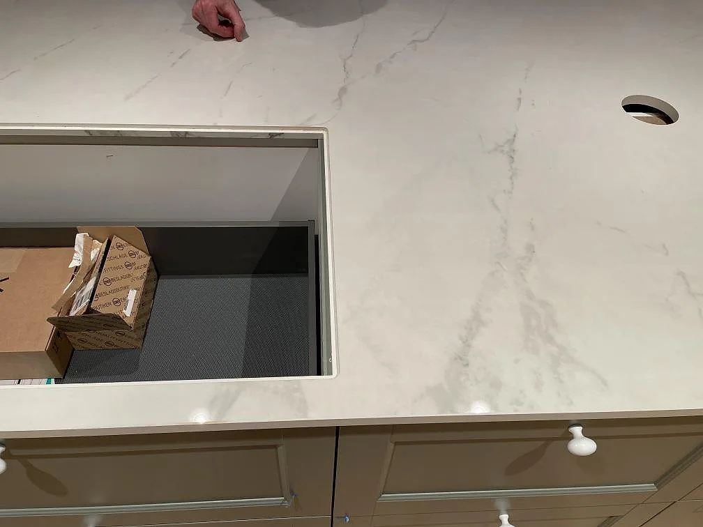 Vit Dekton Tundra bänkskiva med blandarehål och öppet skåp under montering i ett kök i Trelleborg.