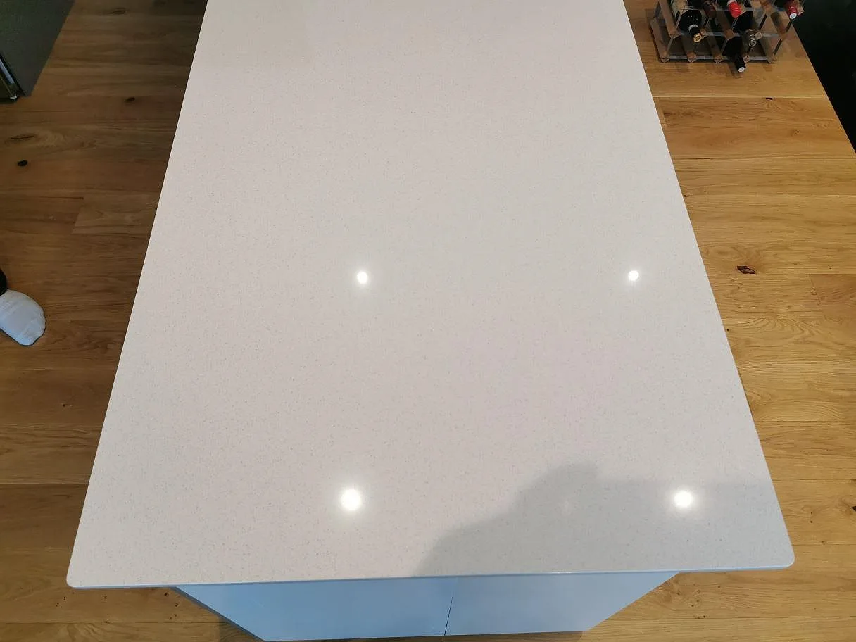 Polerad köksbänkskiva i ljus Dekton Vienna keramik sedd ovanifrån med spegling av takspottar, i ett kök i Kungshamn.