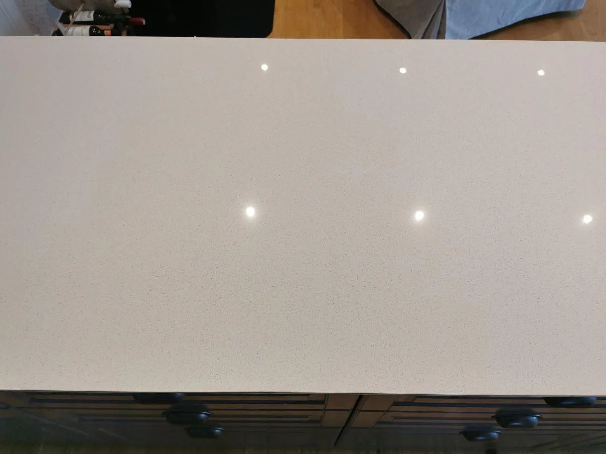 Närbild på den polerade ytan i Dekton Vienna keramik på en köksö med svarta bygelhandtag i ett kök i Kungshamn.